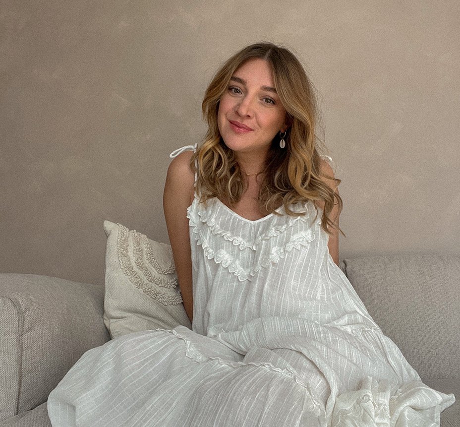 Influencerin Sandra sitzt im weißem Kleid auf einem Sofa