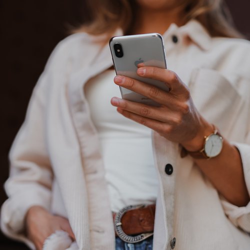 Frau in weißem Hemd hält ein Smartphone in der Hand