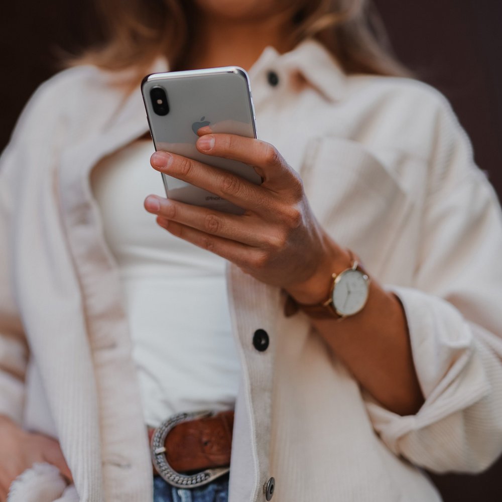 Frau in weißem Hemd hält ein Smartphone in der Hand