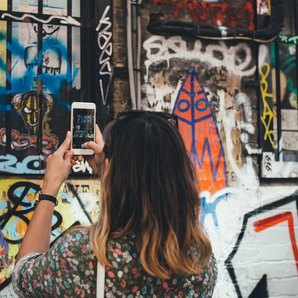 Frau steht vor Graffiti mit Handy